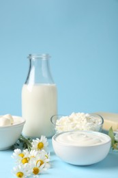 Photo of Fresh dairy products and flowers on light blue background, closeup