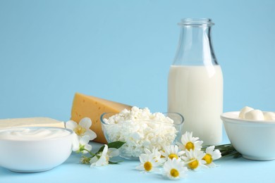 Photo of Fresh dairy products and flowers on light blue background, closeup
