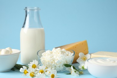 Photo of Fresh dairy products and flowers on light blue background, closeup
