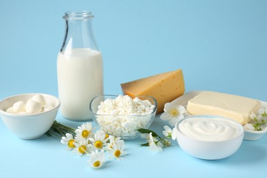 Photo of Fresh dairy products and flowers on light blue background