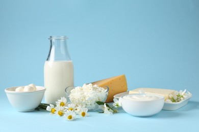 Photo of Fresh dairy products and flowers on light blue background