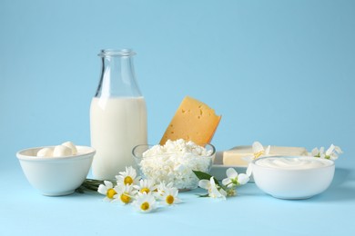Photo of Fresh dairy products and flowers on light blue background