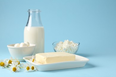 Photo of Fresh dairy products and chamomile flowers on light blue background, closeup