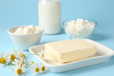 Photo of Fresh dairy products and chamomile flowers on light blue background, closeup