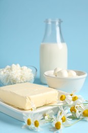 Photo of Fresh dairy products and chamomile flowers on light blue background, closeup