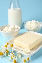 Photo of Fresh dairy products and chamomile flowers on light blue background, closeup