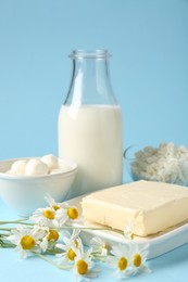 Photo of Fresh dairy products and chamomile flowers on light blue background, closeup