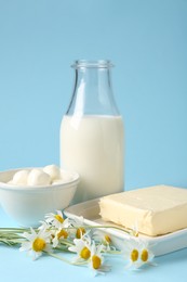 Photo of Fresh dairy products and chamomile flowers on light blue background, closeup
