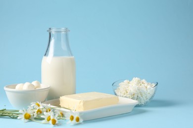 Photo of Fresh dairy products and chamomile flowers on light blue background