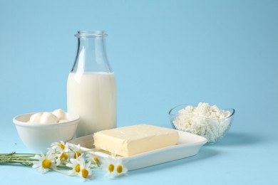Photo of Fresh dairy products and chamomile flowers on light blue background