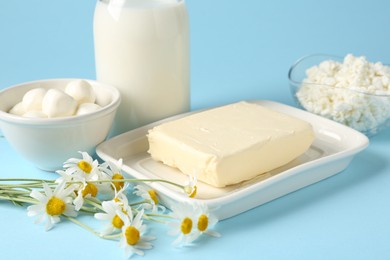 Photo of Fresh dairy products and chamomile flowers on light blue background, closeup