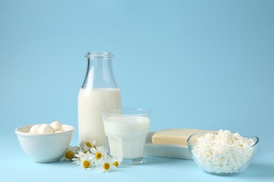 Photo of Fresh dairy products and chamomile flowers on light blue background