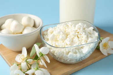 Photo of Fresh dairy products and jasmine flowers on light blue background, closeup