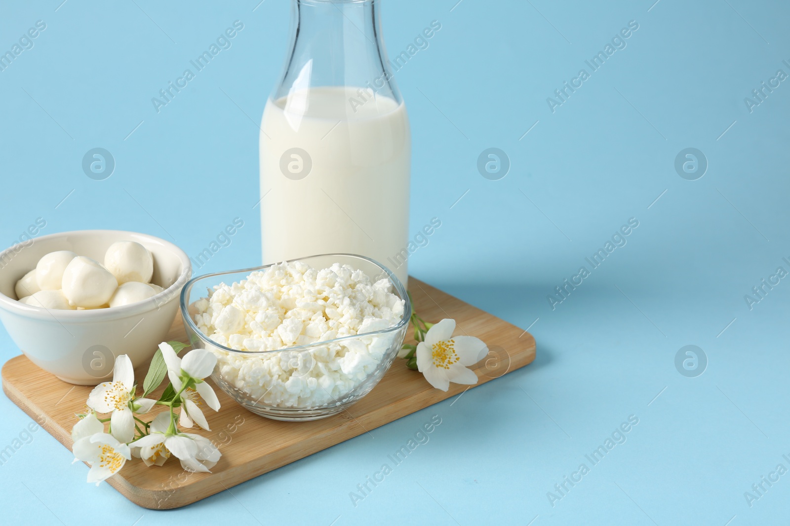 Photo of Fresh dairy products and jasmine flowers on light blue background, closeup. Space for text
