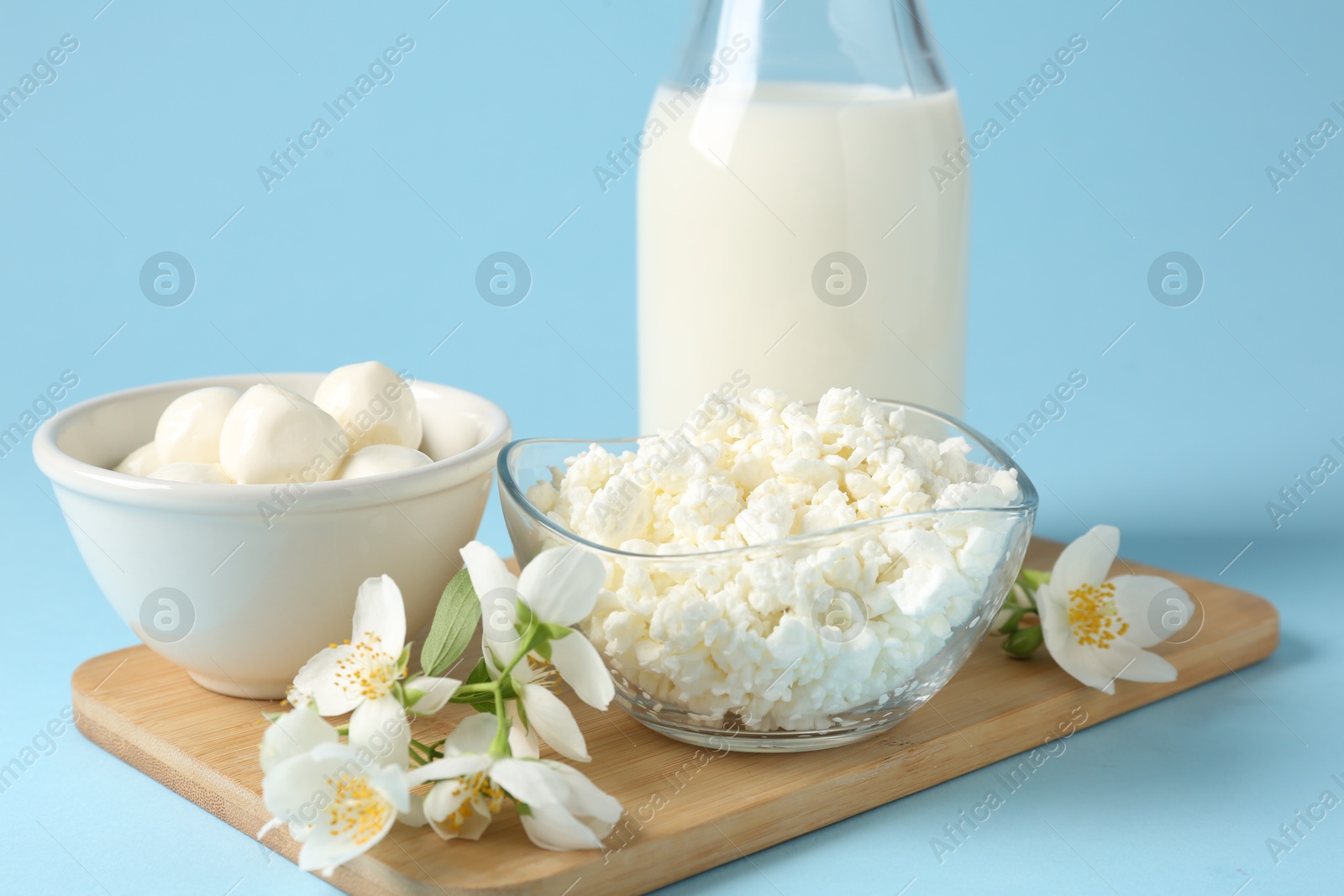 Photo of Fresh dairy products and jasmine flowers on light blue background, closeup