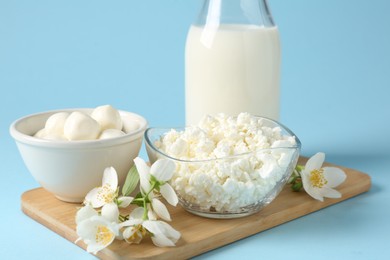 Photo of Fresh dairy products and jasmine flowers on light blue background, closeup