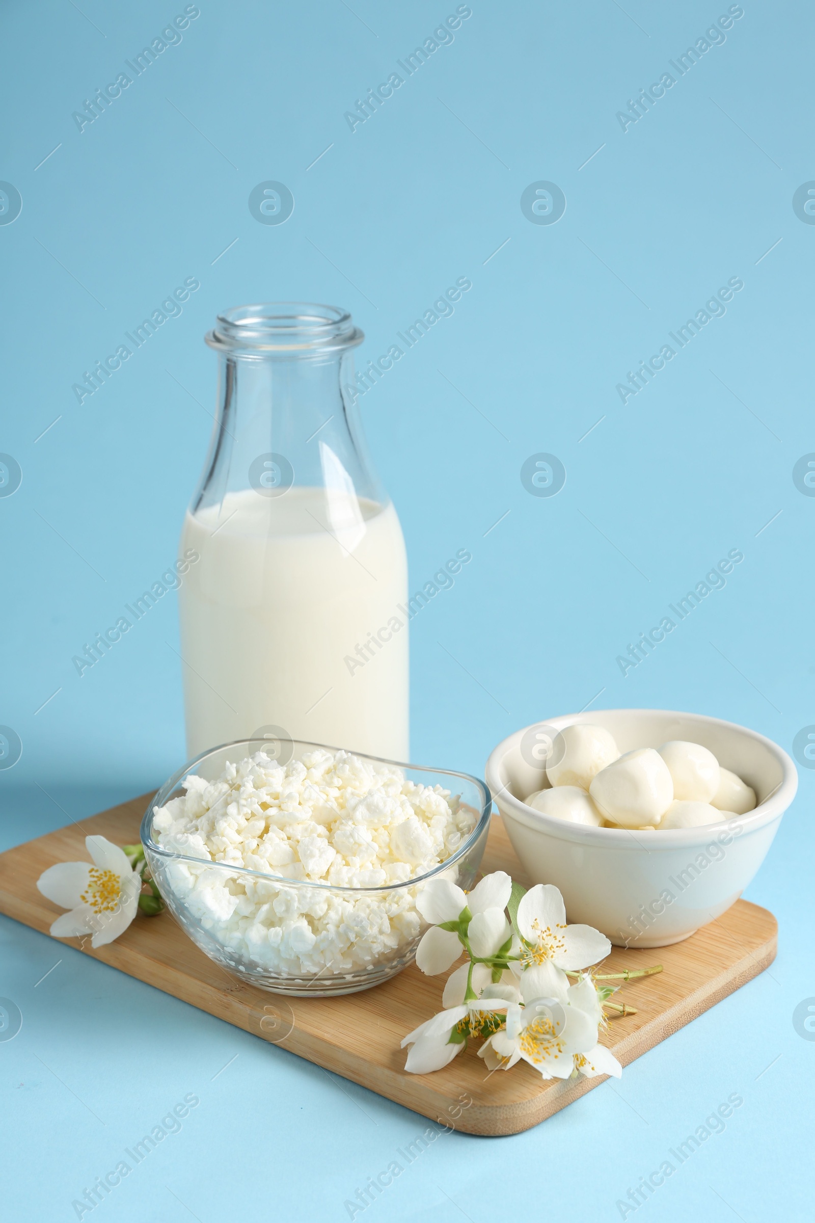 Photo of Fresh dairy products and jasmine flowers on light blue background