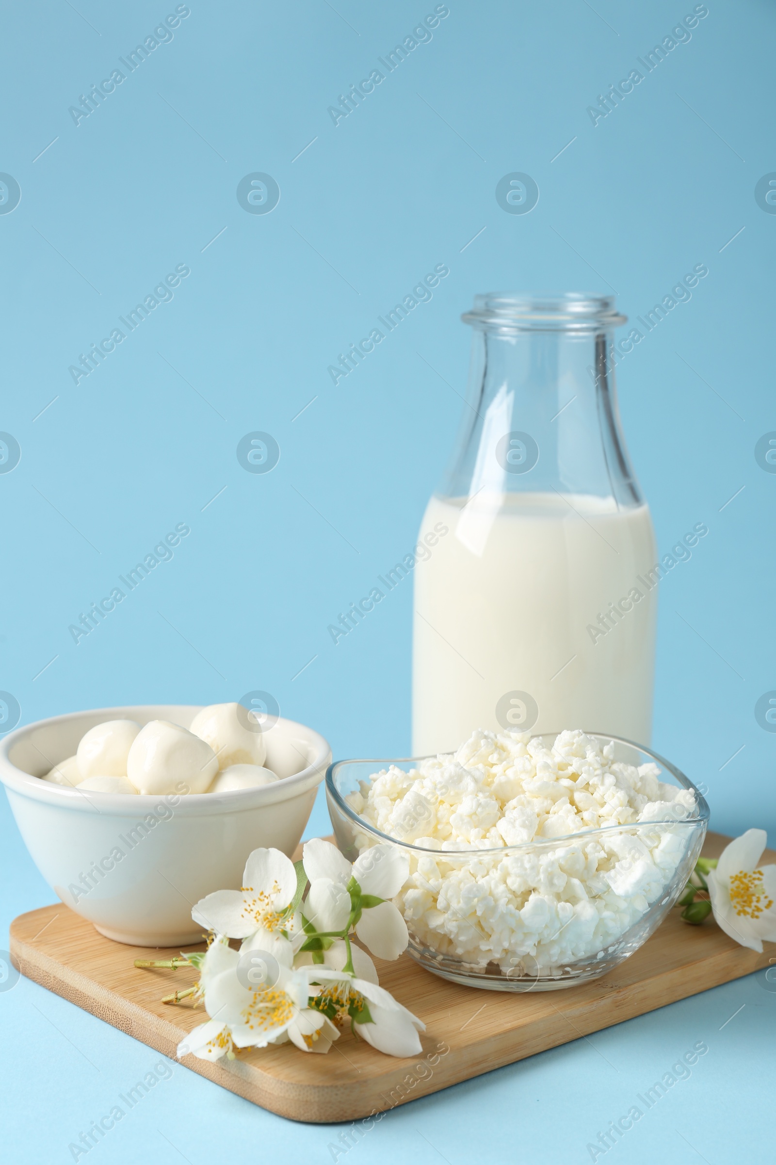 Photo of Fresh dairy products and jasmine flowers on light blue background, closeup