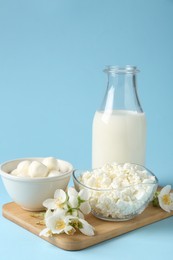 Photo of Fresh dairy products and jasmine flowers on light blue background, closeup