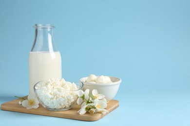 Photo of Fresh dairy products and jasmine flowers on light blue background. Space for text