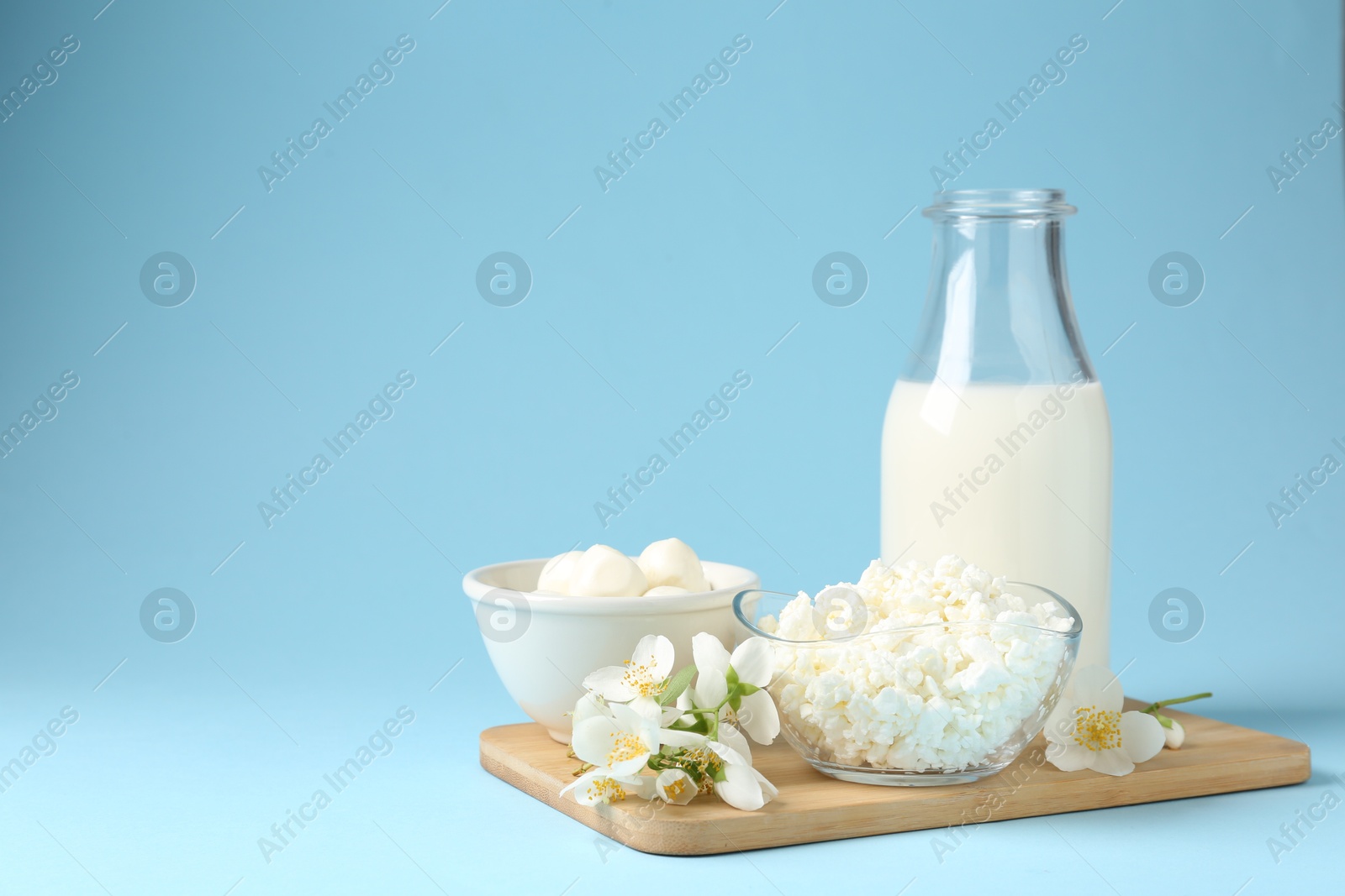Photo of Fresh dairy products and jasmine flowers on light blue background. Space for text