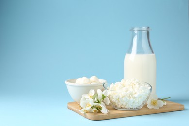 Photo of Fresh dairy products and jasmine flowers on light blue background. Space for text
