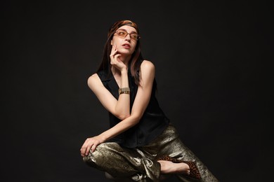 Photo of Beautiful woman in stylish outfit sitting on chair against black background