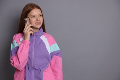 Photo of Smiling teenage girl talking by smartphone on grey background. Space for text