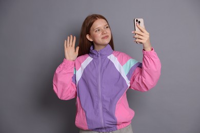 Photo of Beautiful teenage girl having videocall by smartphone on grey background