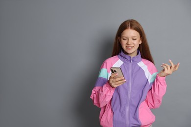 Photo of Smiling teenage girl with smartphone on grey background. Space for text