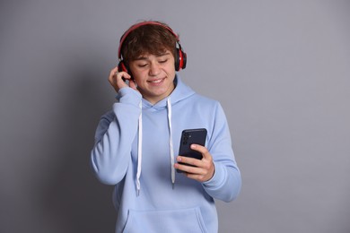 Photo of Smiling teenage boy in headphones using smartphone on grey background