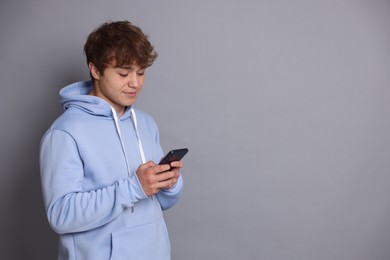 Photo of Teenage boy using smartphone on grey background. Space for text
