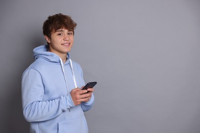 Photo of Smiling teenage boy with smartphone on grey background. Space for text