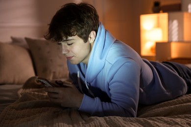 Photo of Teenage boy using smartphone on bed at home