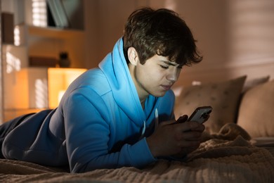 Photo of Teenage boy using smartphone on bed at home
