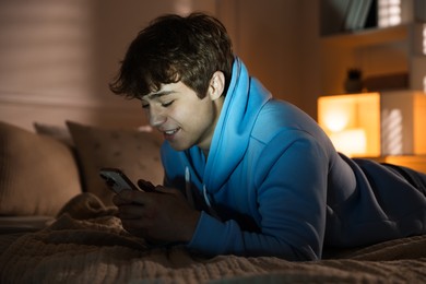 Photo of Smiling teenage boy using smartphone on bed at home