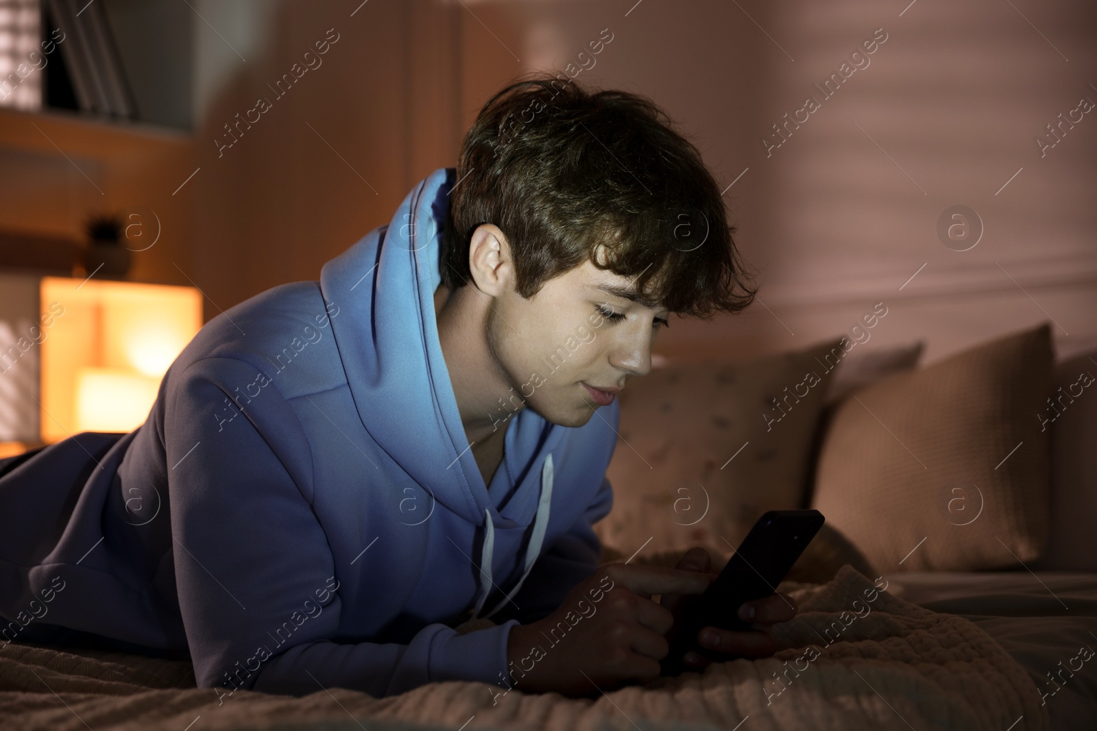 Teenage boy using smartphone on bed at home Photo of Teenage boy using smartphone on bed at home