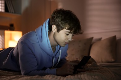 Photo of Teenage boy using smartphone on bed at home