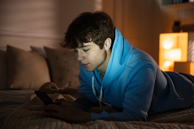 Photo of Teenage boy using smartphone on bed at home