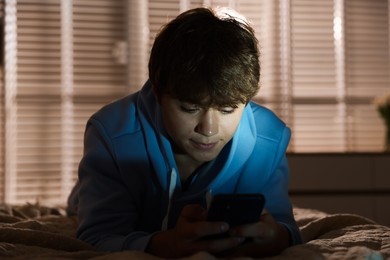Photo of Teenage boy using smartphone on bed at home