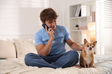 Photo of Smiling teenage boy talking by smartphone and dog on bed at home
