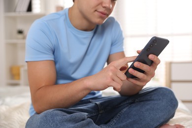 Photo of Teenage boy using smartphone on bed at home, closeup