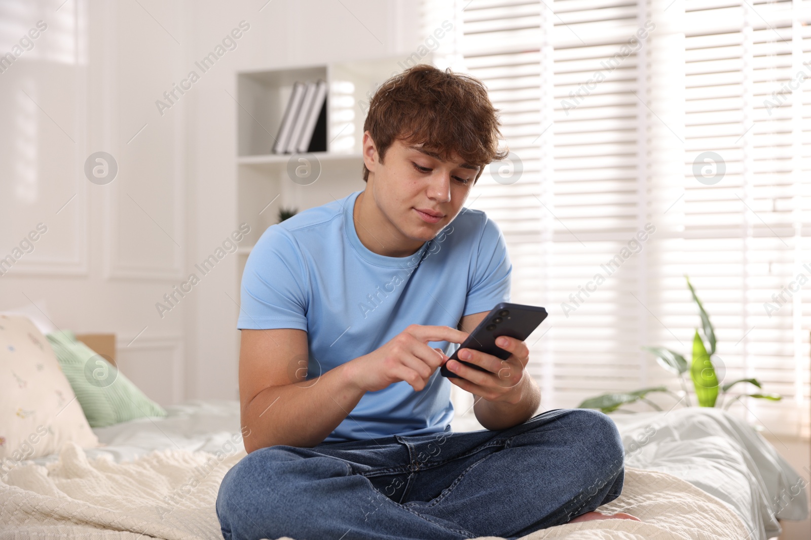 Photo of Teenage boy using smartphone on bed at home