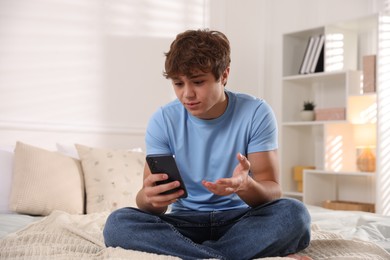 Photo of Teenage boy having videocall by smartphone on bed at home