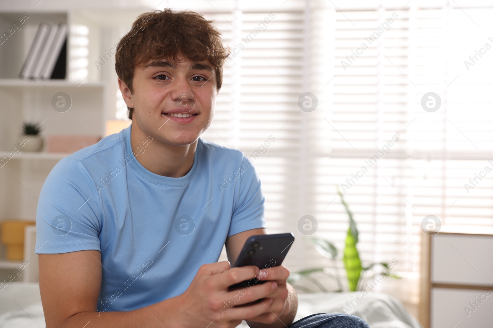 Photo of Smiling teenage boy using smartphone at home