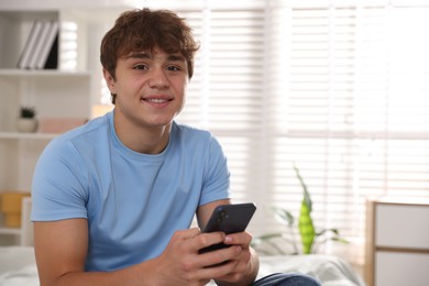 Photo of Smiling teenage boy using smartphone at home