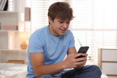 Photo of Smiling teenage boy using smartphone on bed at home