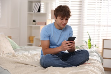 Photo of Teenage boy using smartphone on bed at home