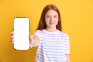 Photo of Beautiful teenage girl showing smartphone with blank screen on yellow background, selective focus. Mockup for design