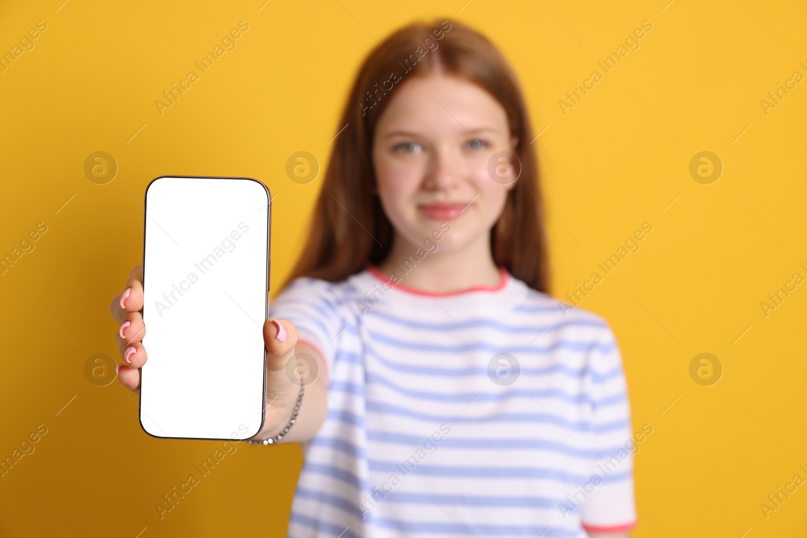 Photo of Beautiful teenage girl showing smartphone with blank screen on yellow background, selective focus. Mockup for design